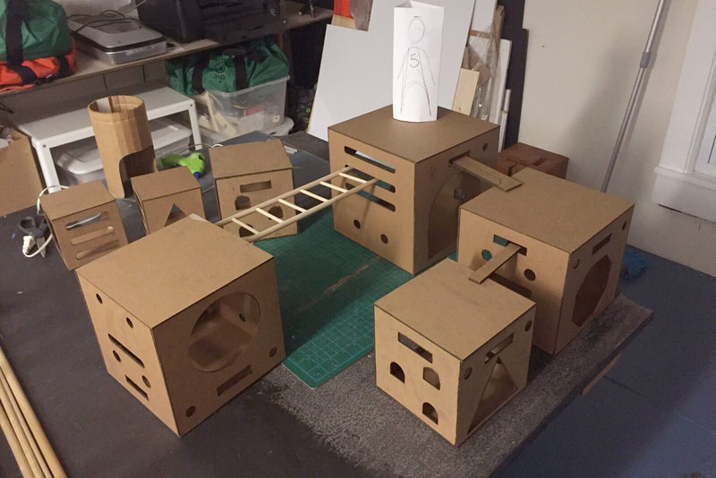 Scale models of Anji Play climbing cubes made from chipboard. They are arranged on a desktop, creating a play structure in miniature.