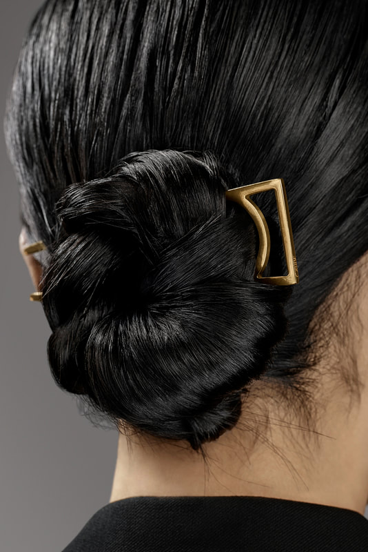 Promotional image of a model wearing a gold plated Oribe hair stick.
